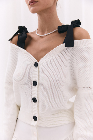 Short knitted cardigan with open shoulders and buttons. The straps on the shoulders are tied into elegant bows, creating a delicate and feminine look. Ideal for creating fashionable autumn looks.