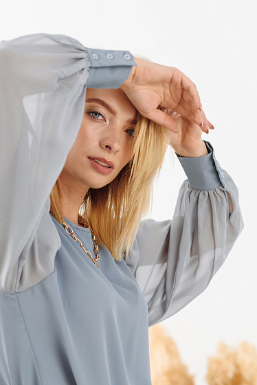 Блузка з струмуючої тканини, ззаду застібається на гудзик, прямий крій, круглий виріз горловини, широкий, об'ємний шифоновий рукав зі складанням по плечу, високі манжети з ґудзиками.