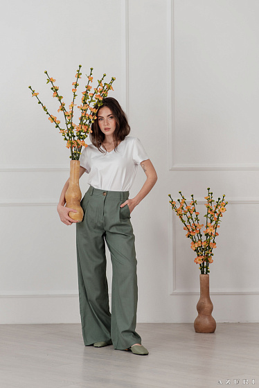 Льняные брюки с высокой посадкой и широкими штанинами. Спереди защипы, по бокам карманы, застегиваются на змейку и пуговицу.